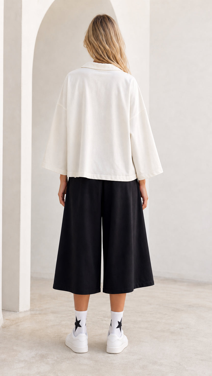 Back view of model wearing white relaxed fit open collar shirt and cropped wide leg pants