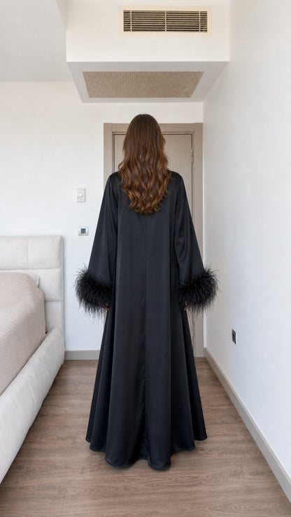 Back view of model in long flowing black satin maxi dress with feather trims