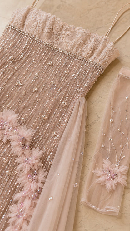Close-up of blush gown beadwork, lace-like bodice detail, floral appliqué, and sheer sleeve accessory