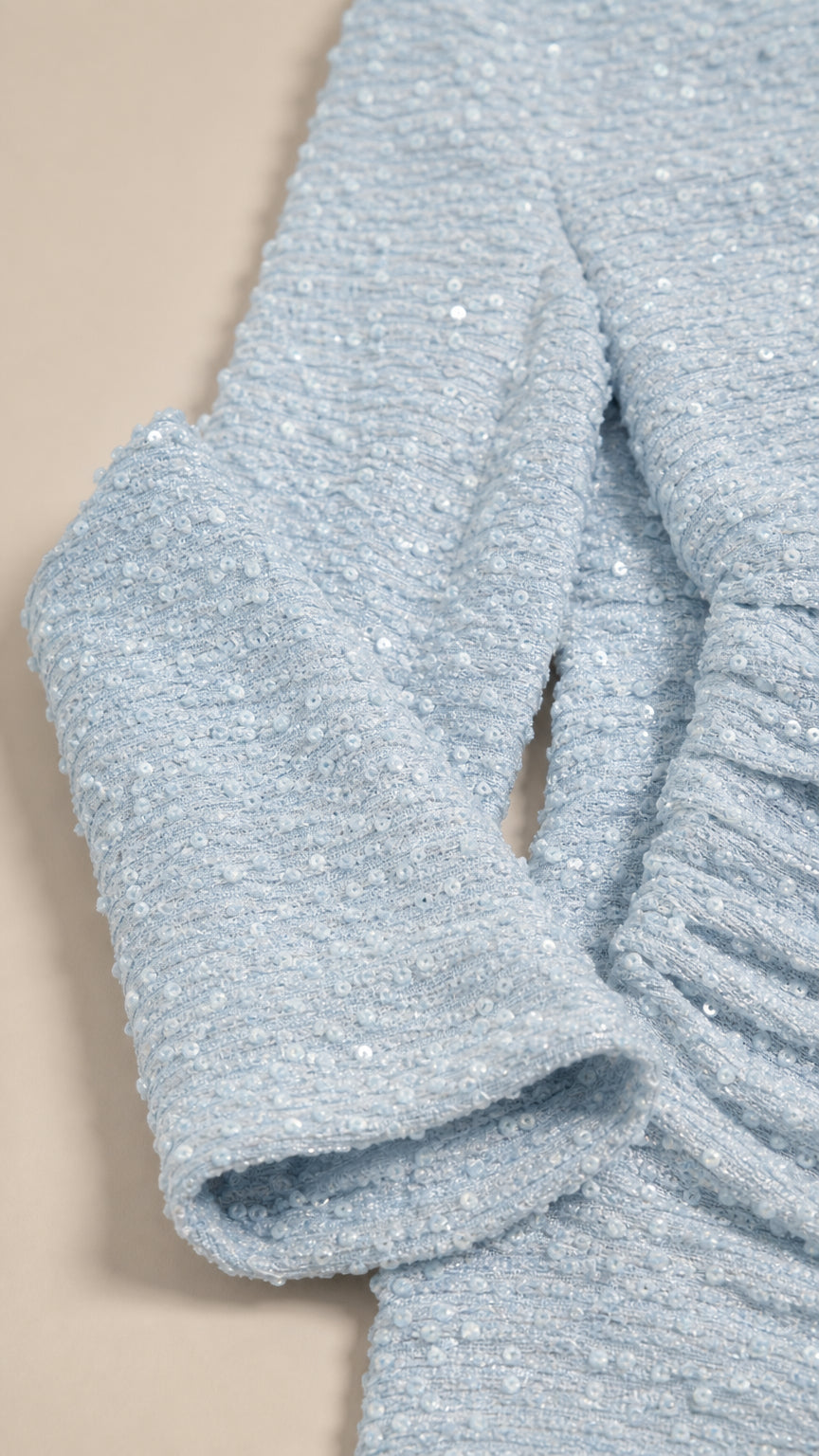 Close-up detail of textured knit fabric with subtle sequin shimmer on sleeve cuff