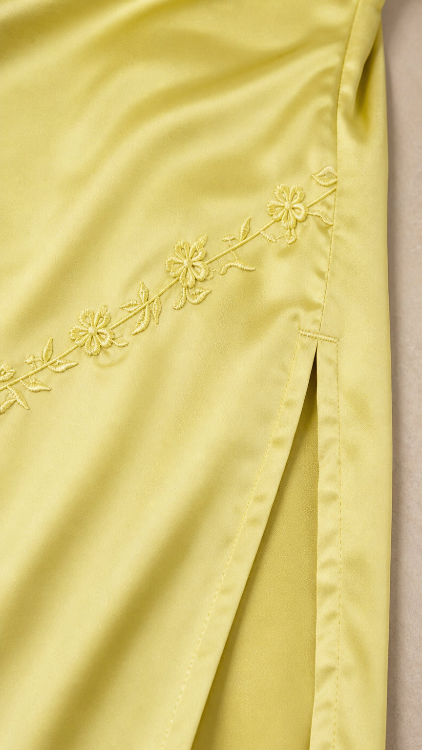 Close-up detail of tonal floral embroidery along diagonal seam on satin maxi dress