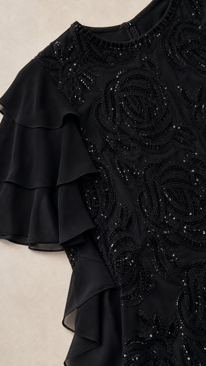 Close-up detail of black dress beadwork and ruffle sleeve