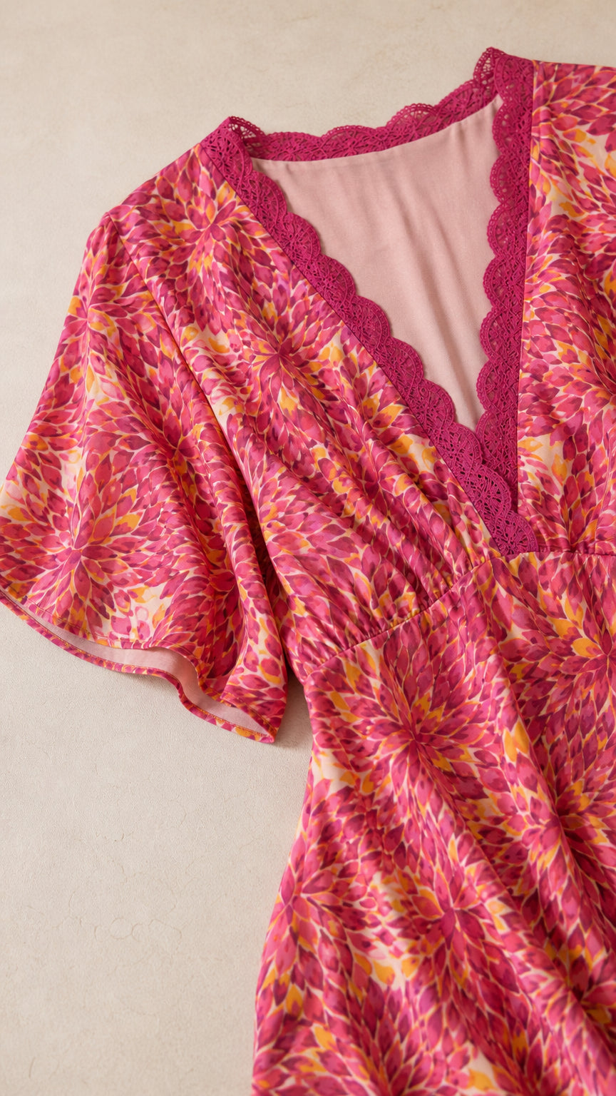 Close-up detail of fuchsia pink dress showing V-neckline crochet lace trim and sleeve drape