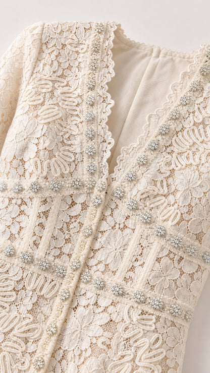 Close-up detail of textured ivory lace fabric, scalloped V-neck, and crystal bead trim