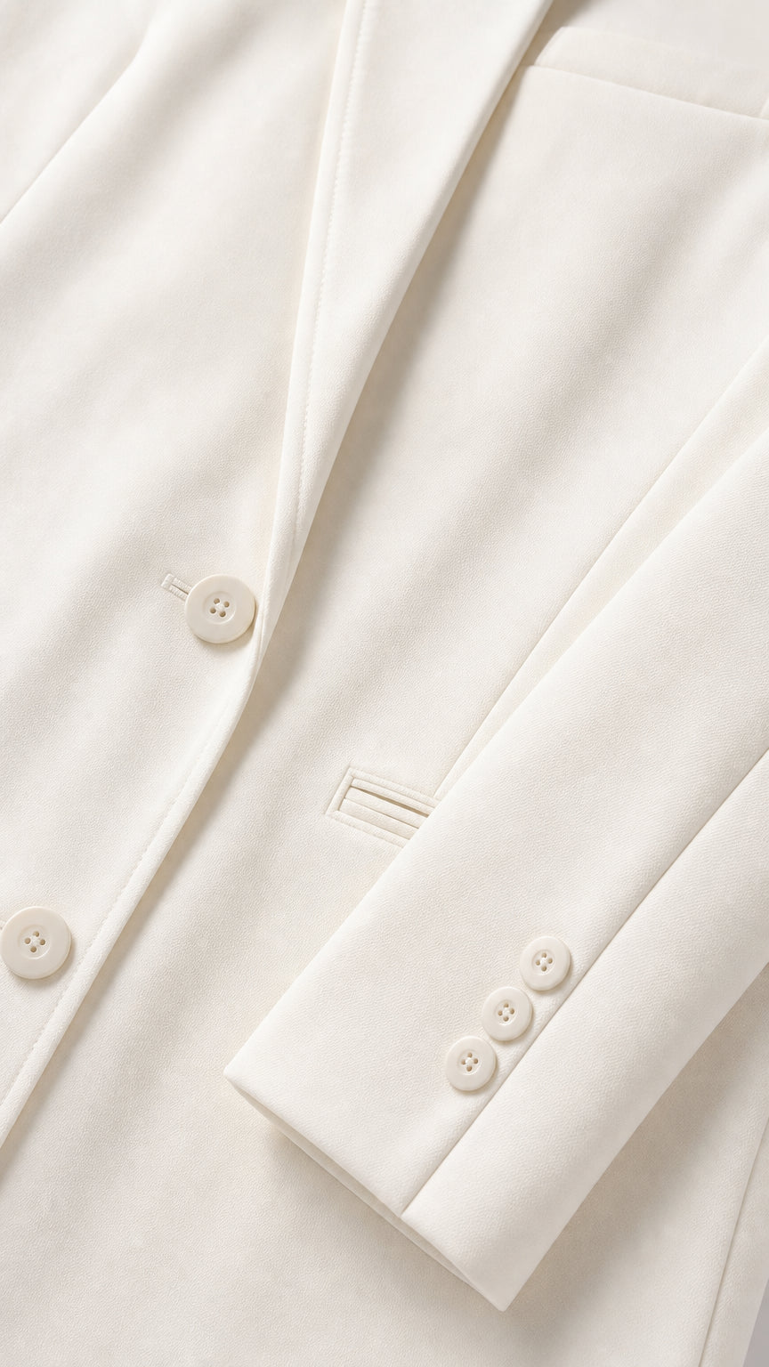 Close-up detail of smooth ivory fabric, lapel seam, tonal front button, and three-button sleeve cuff