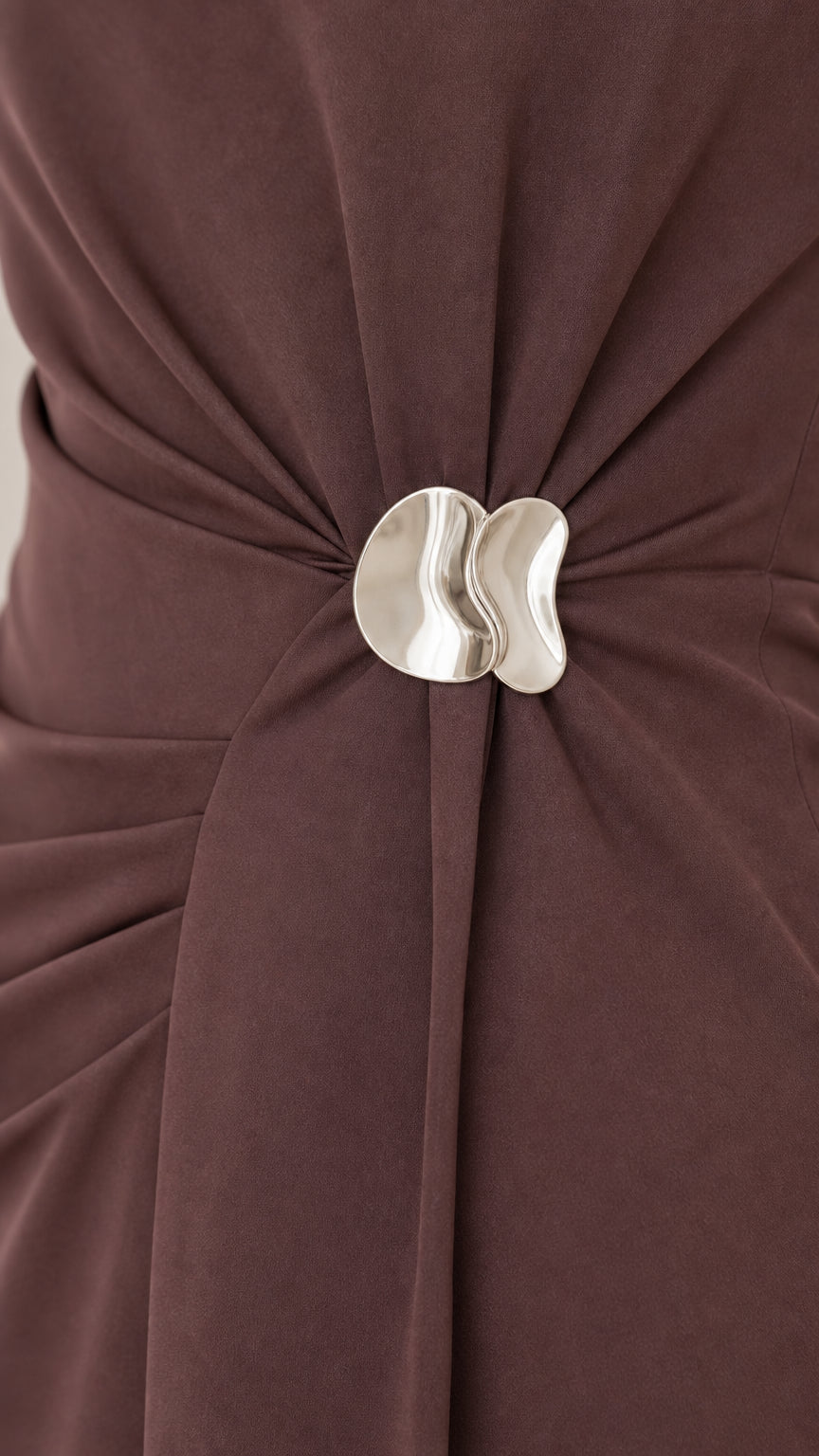Close-up detail of gathered waist pleats with sculptural silver metallic buckle on brown dress