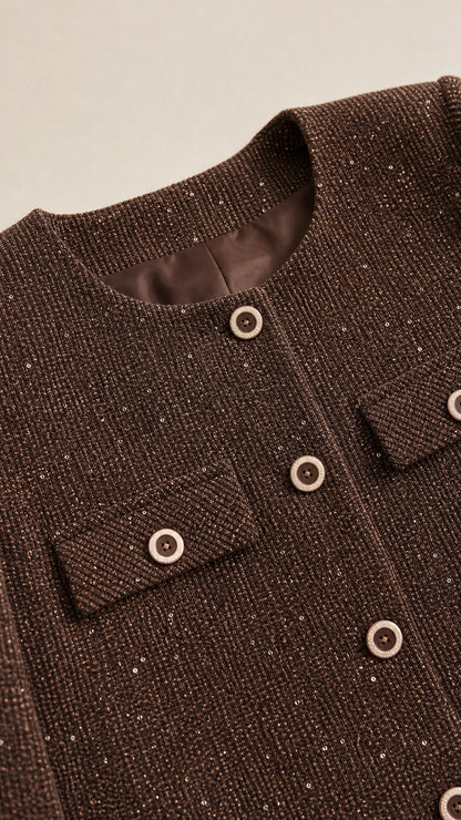 Close-up detail of textured brown tweed fabric, contrasting buttons, and pocket flap