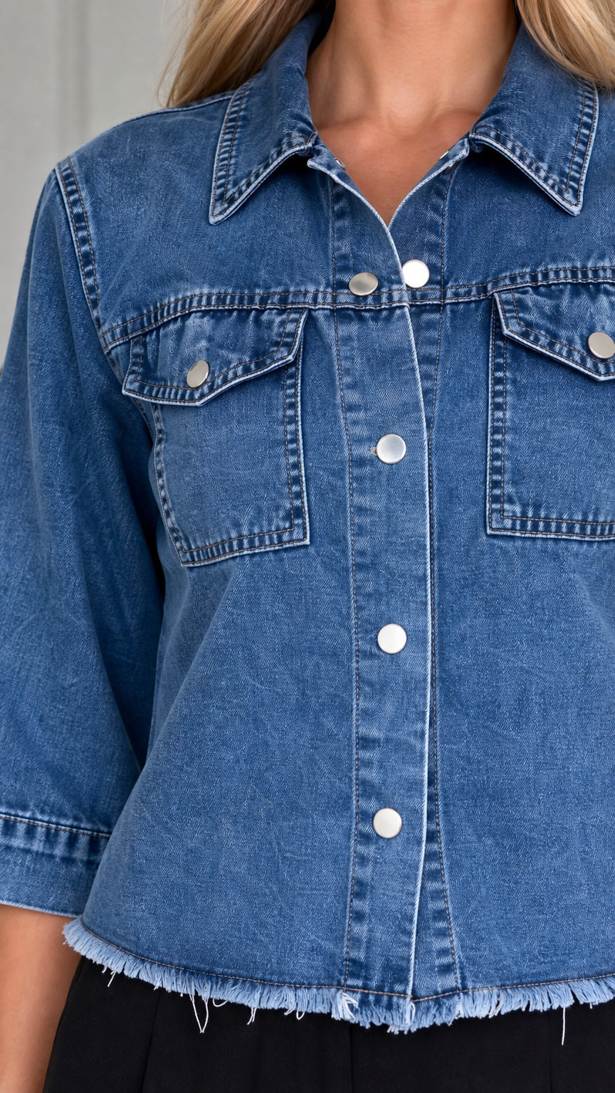 Close-up of front button closure, chest pockets, and raw hem of blue denim shirt