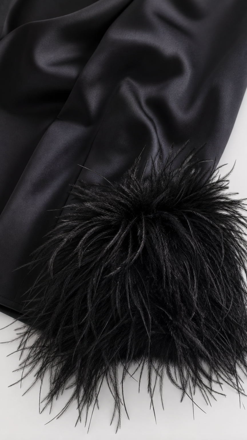 Close-up detail of smooth black satin fabric and voluminous fluffy feather cuff trim