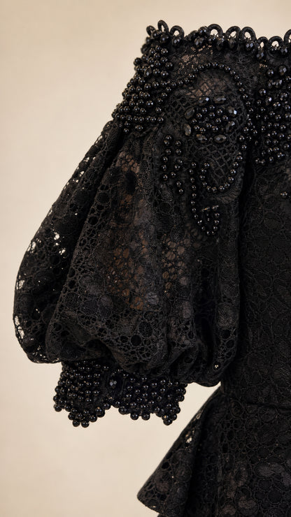 Close-up detail of black floral lace fabric with intricate beadwork along the sleeve cuff and neckline