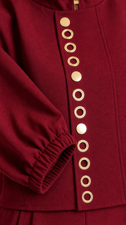 Close-up detail of gold-tone button and eyelet trim on burgundy top and sleeve cuff