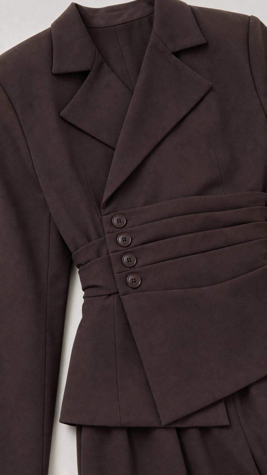 Close-up detail of chocolate brown asymmetric pleated blazer with covered buttons and lapel