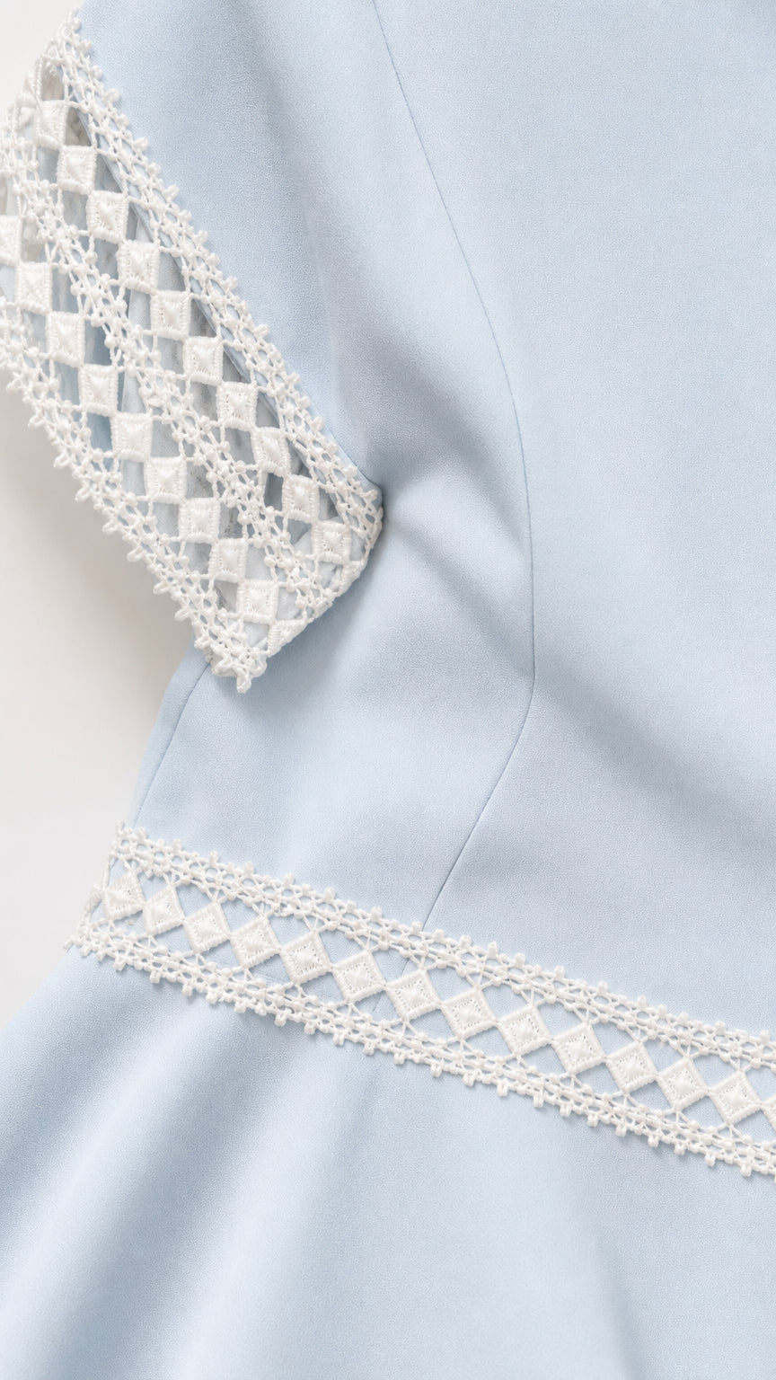 Close-up detail of geometric diamond openwork crochet lace trim on sleeve and waistband