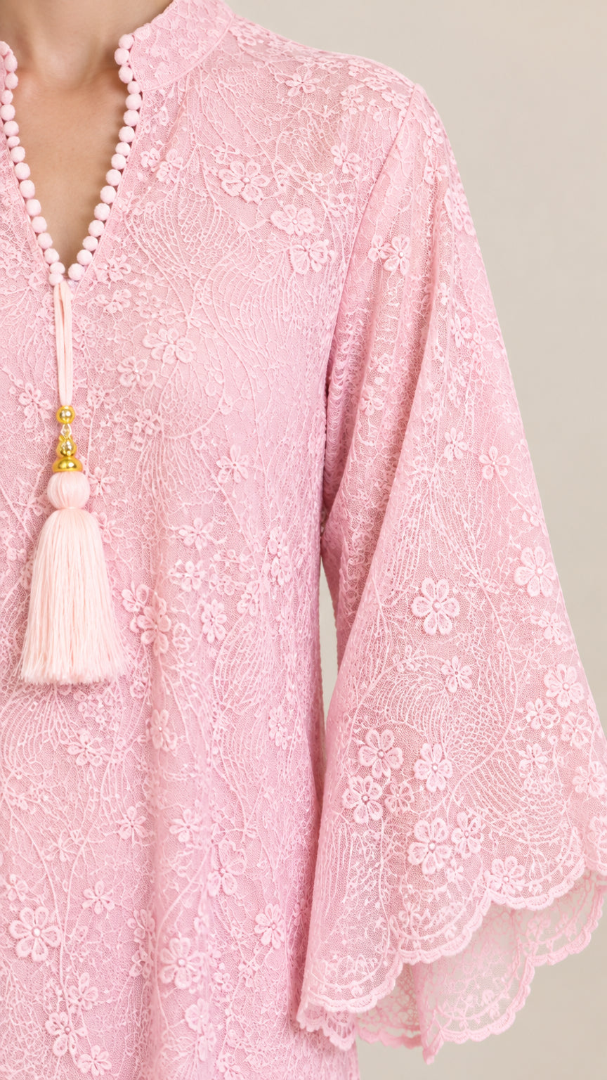 Close-up detail of pink floral lace fabric, beaded neckline, and tassel accent