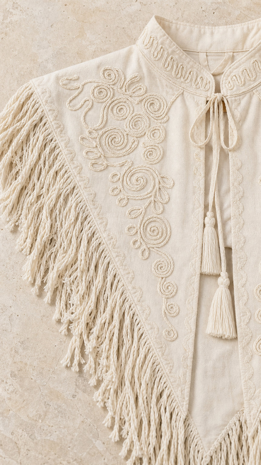 Close-up detail of intricate soutache scroll embroidery and tassel fringe on cream fabric