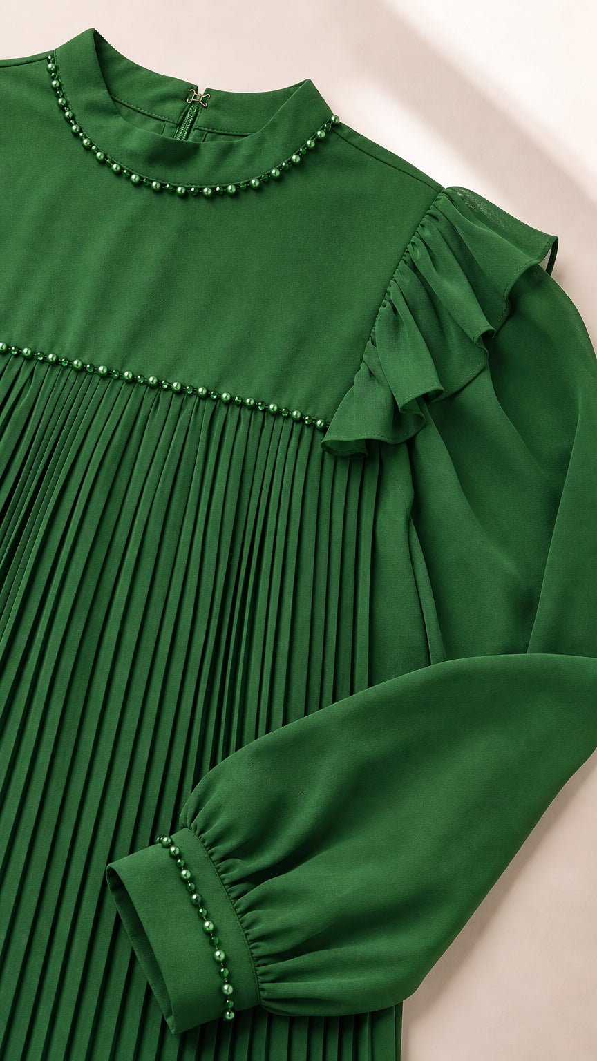 Close-up detail of beaded mock neckline, shoulder ruffles, and beaded cuff on green pleated dress
