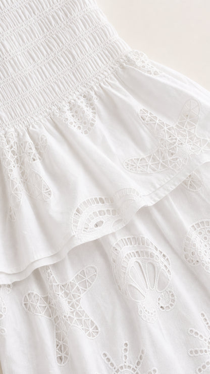 Close-up detail of smocked bodice and embroidered fabric on white dress