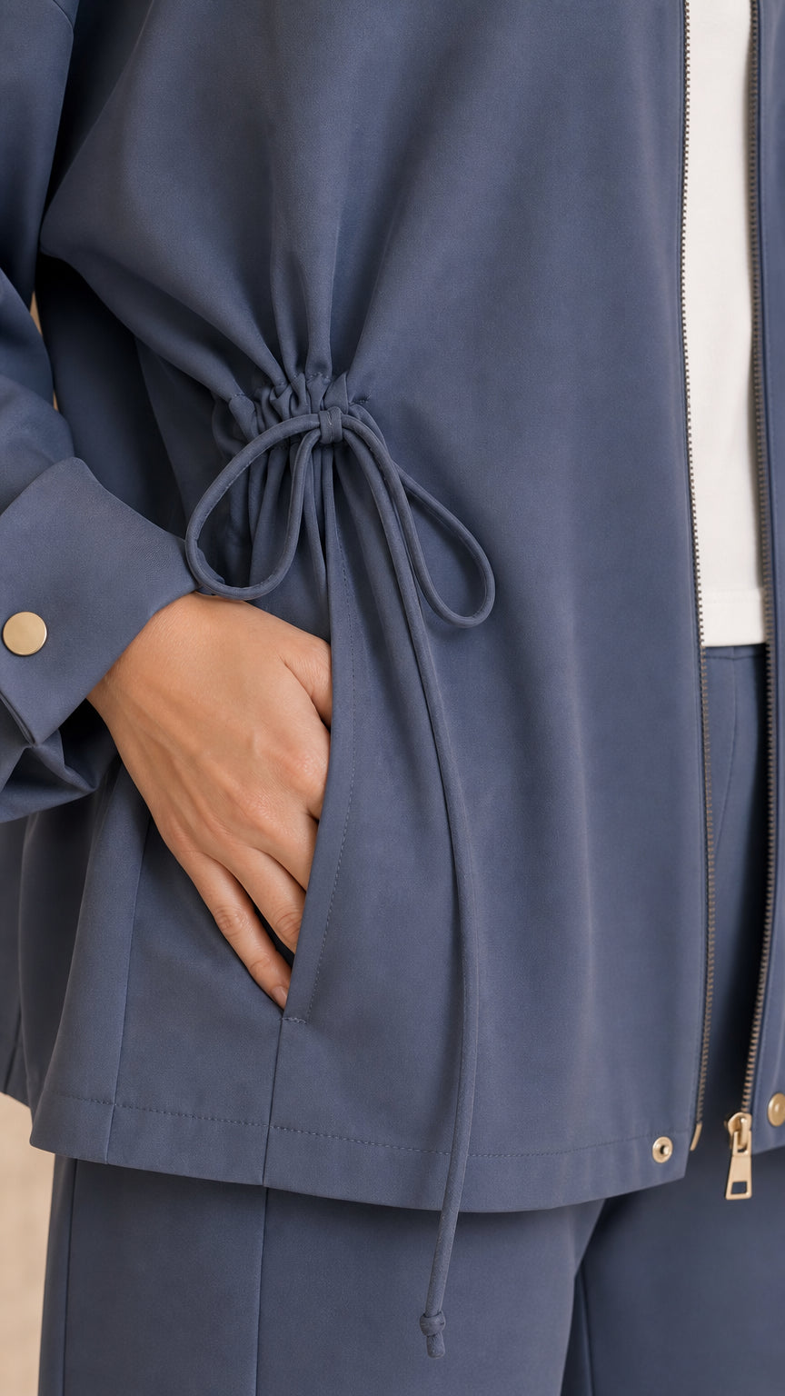 Close-up detail of Slate Blue jacket showing side drawstring tie, pocket, and zipper