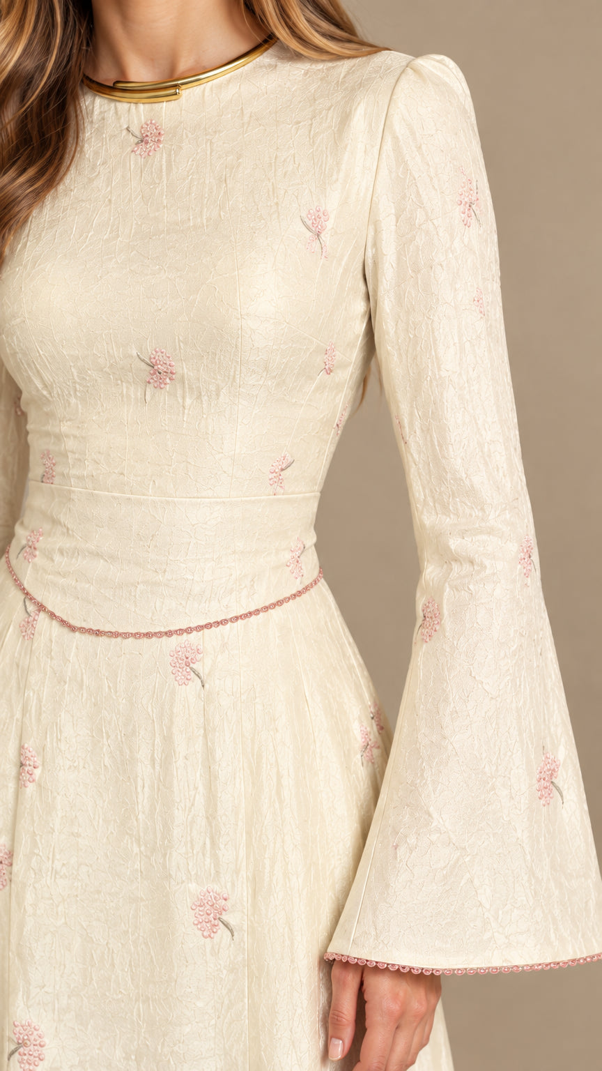 Close-up detail of cream textured jacquard fabric with floral motifs and bell sleeves
