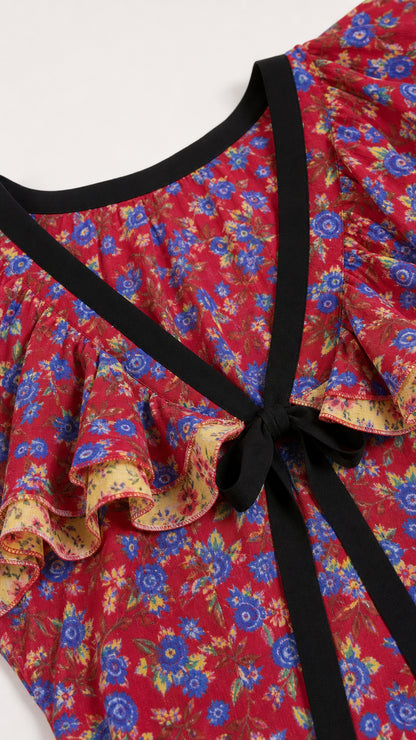 Close-up detail of neckline showing ruffle trim and black tie on red floral fabric