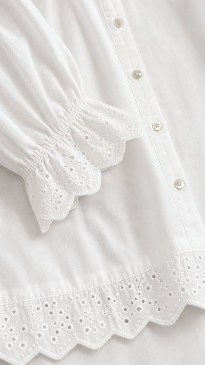 Close-up detail of white eyelet embroidered lace trim, scalloped hem, and buttons