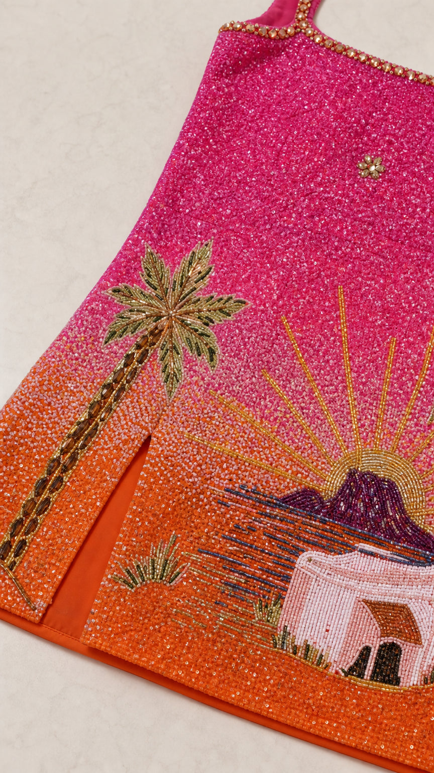 Close-up detail of hand-beaded palm tree, sunset rays, and slit hem
