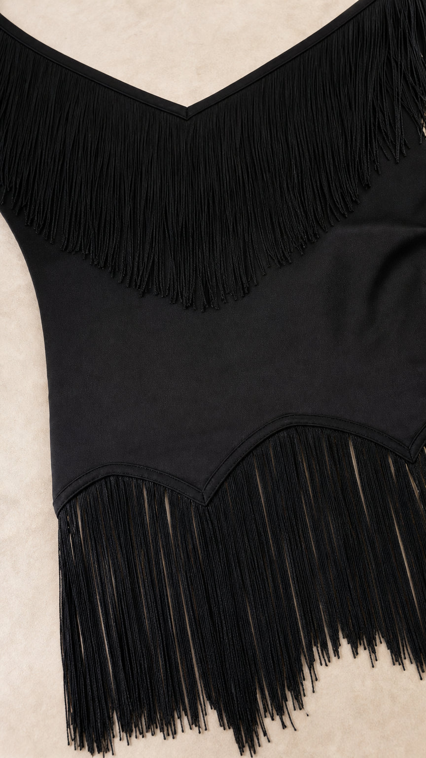 Close-up detail of black fabric and layered fringe trimming at neckline and hem