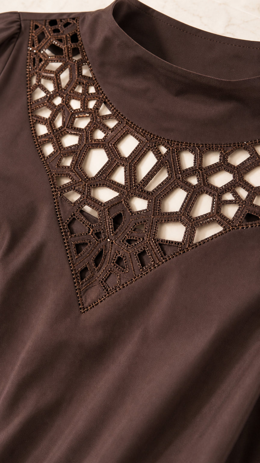 Close-up detail of geometric laser cutout collar and neckline on brown top