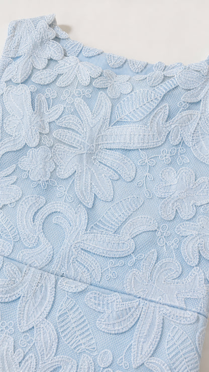 Close-up detail of embroidered floral lace fabric texture in light blue
