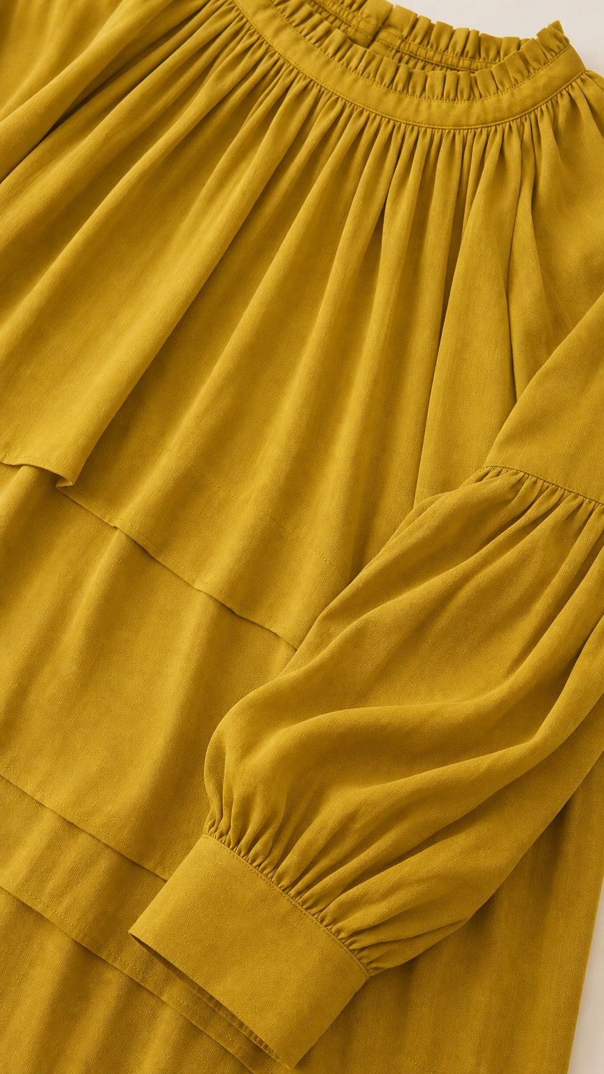 Close-up detail of gathered neckline and pleated texture on mustard dress