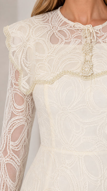 Close-up detail of the pearl-trimmed capelet, neck tie tassel, and sheer lace bodice