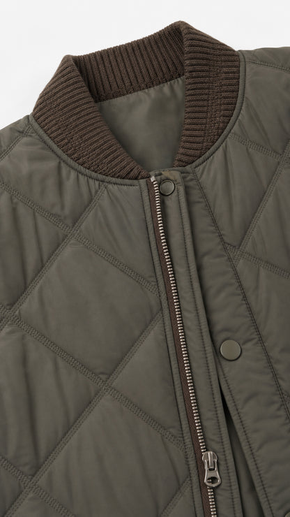 Close-up detail of olive green quilted fabric, ribbed neckline, and metal zipper