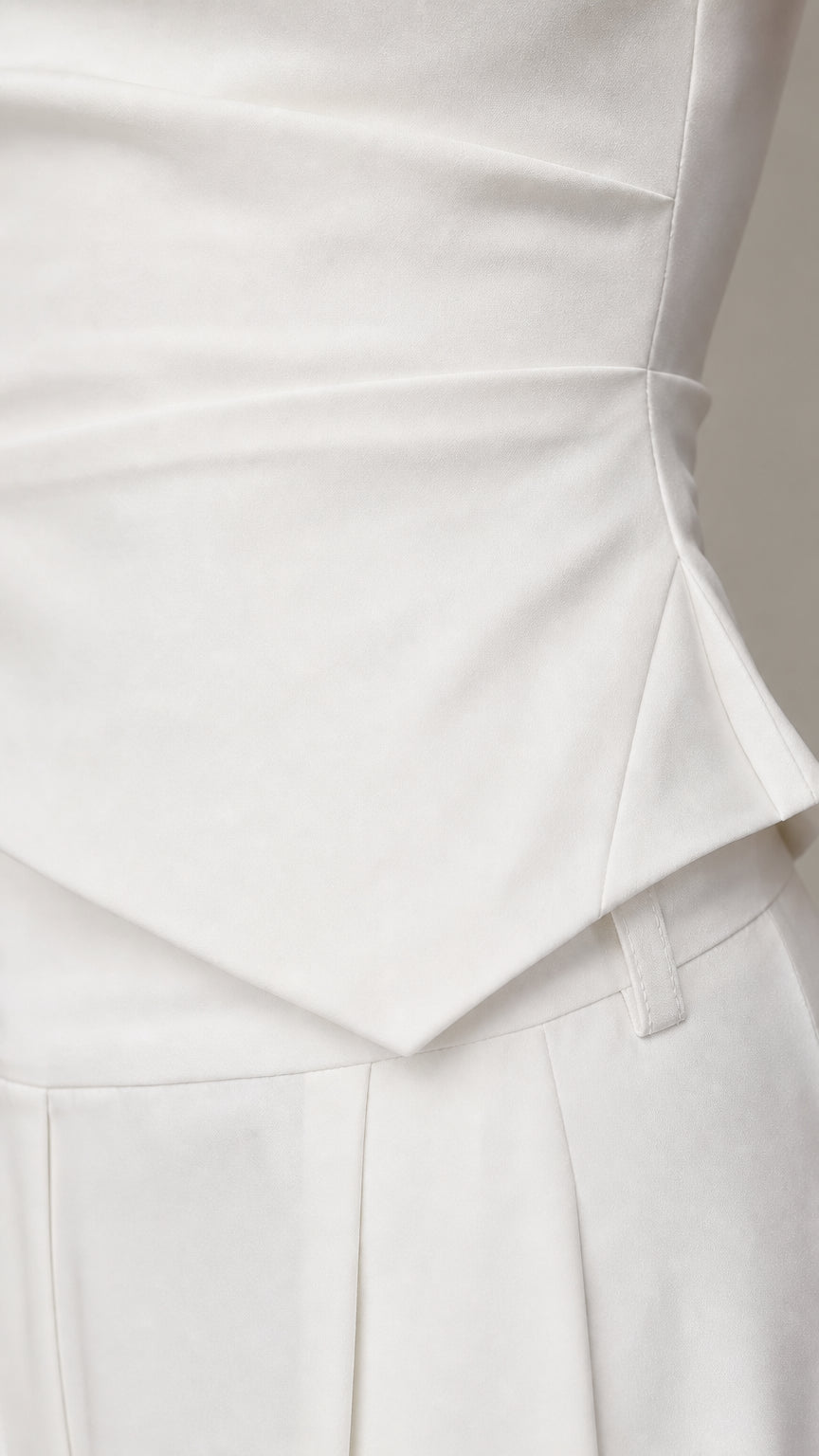 Close-up detail of the asymmetric draped peplum waist and trousers