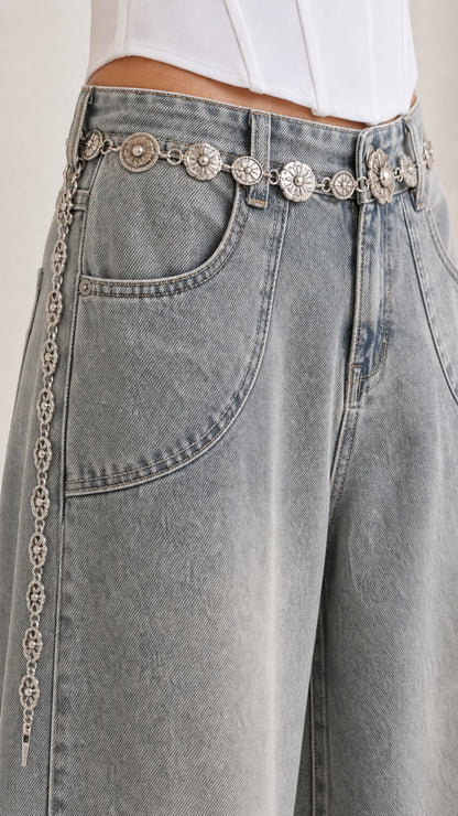 Close-up detail of curved front pocket and waistband on washed grey denim jeans