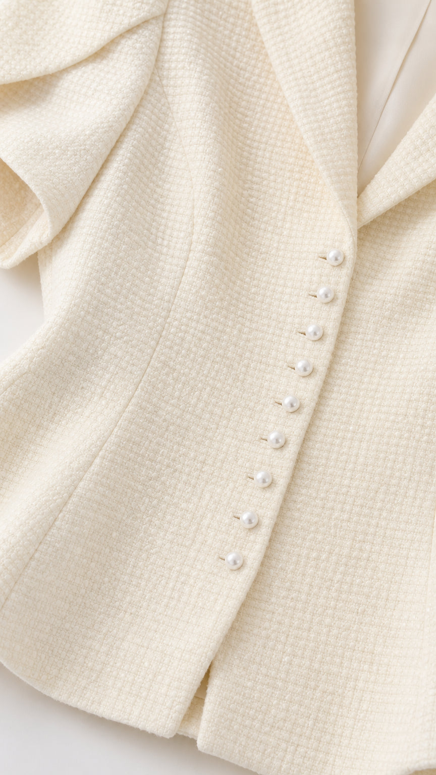 Close-up detail of textured ivory tweed fabric and faux pearl buttons on peplum blazer