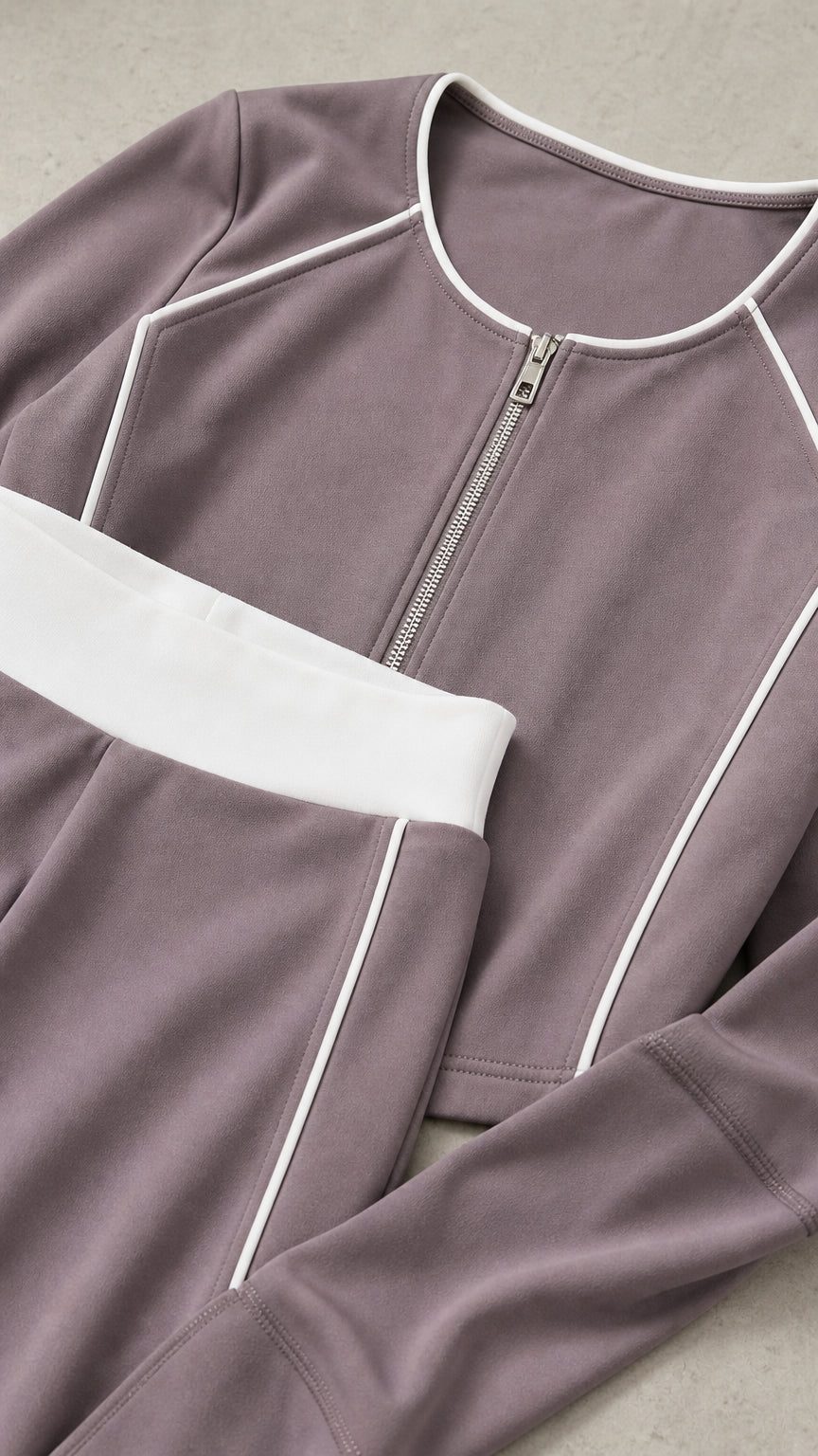 Close-up flat lay of dusty mauve cropped zip jacket and pants waistband showing white piping details