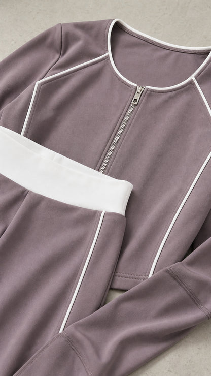 Close-up flat lay of dusty mauve cropped zip jacket and pants waistband showing white piping details