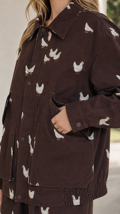 Close-up detail of brown utility jacket showing intricate chicken embroidery and pocket detail