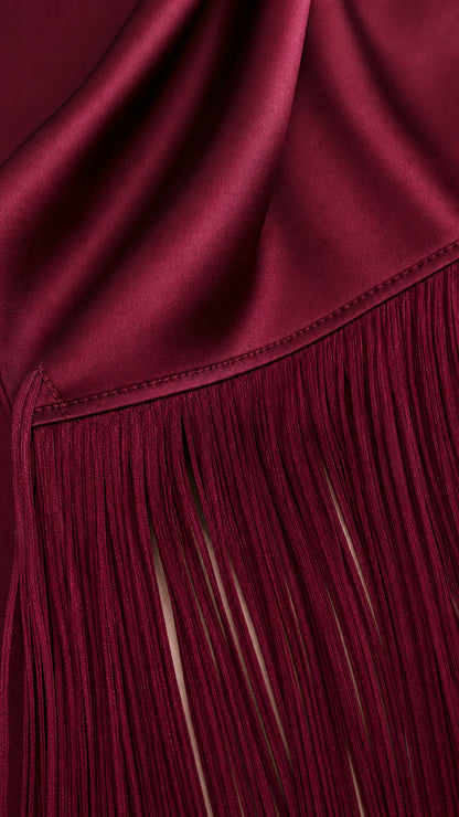 Close-up detail of burgundy satin fabric seam and fine fringe trim