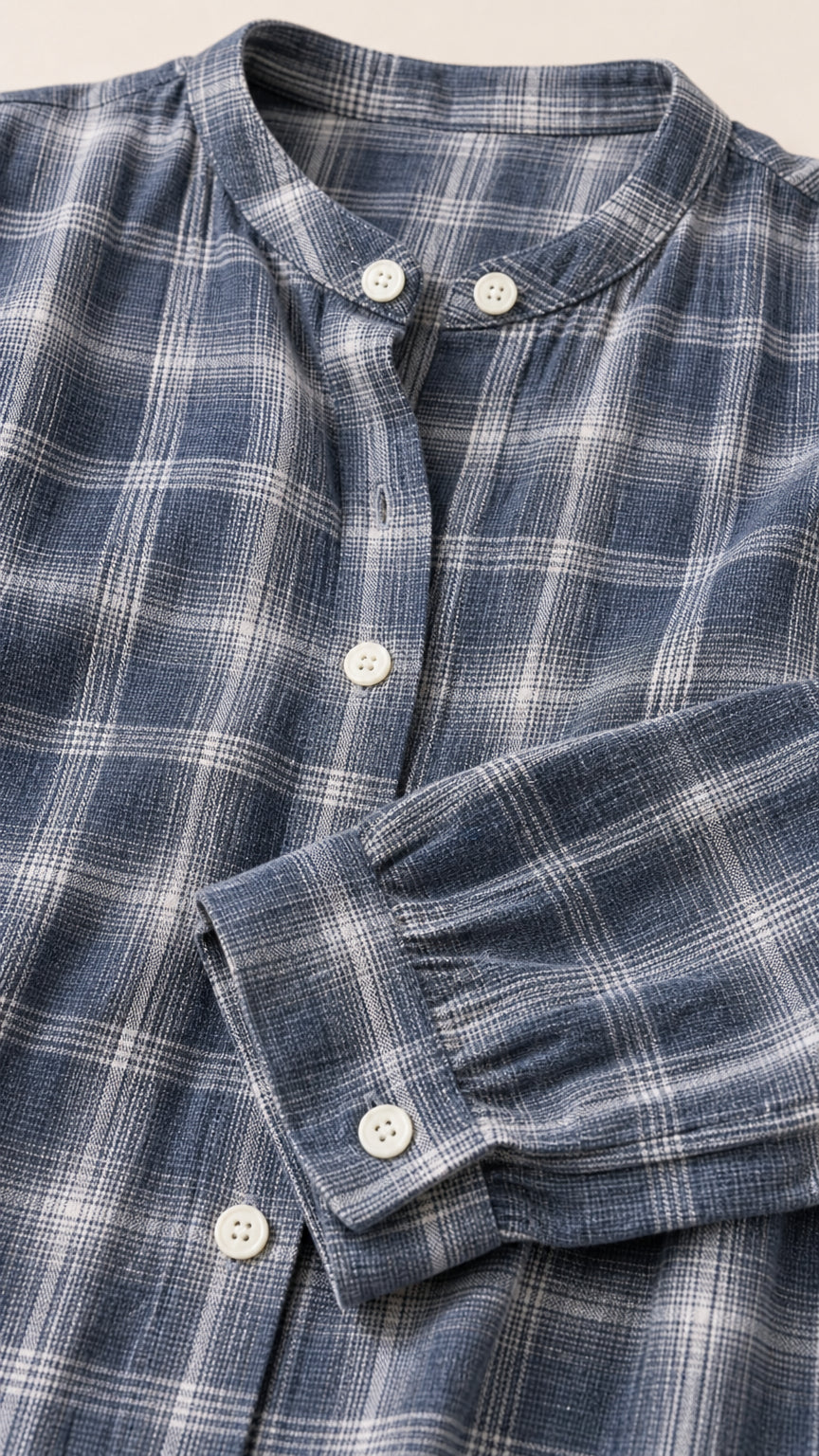 Close-up detail of mandarin band collar, front buttons, and cuff on slate blue plaid woven fabric