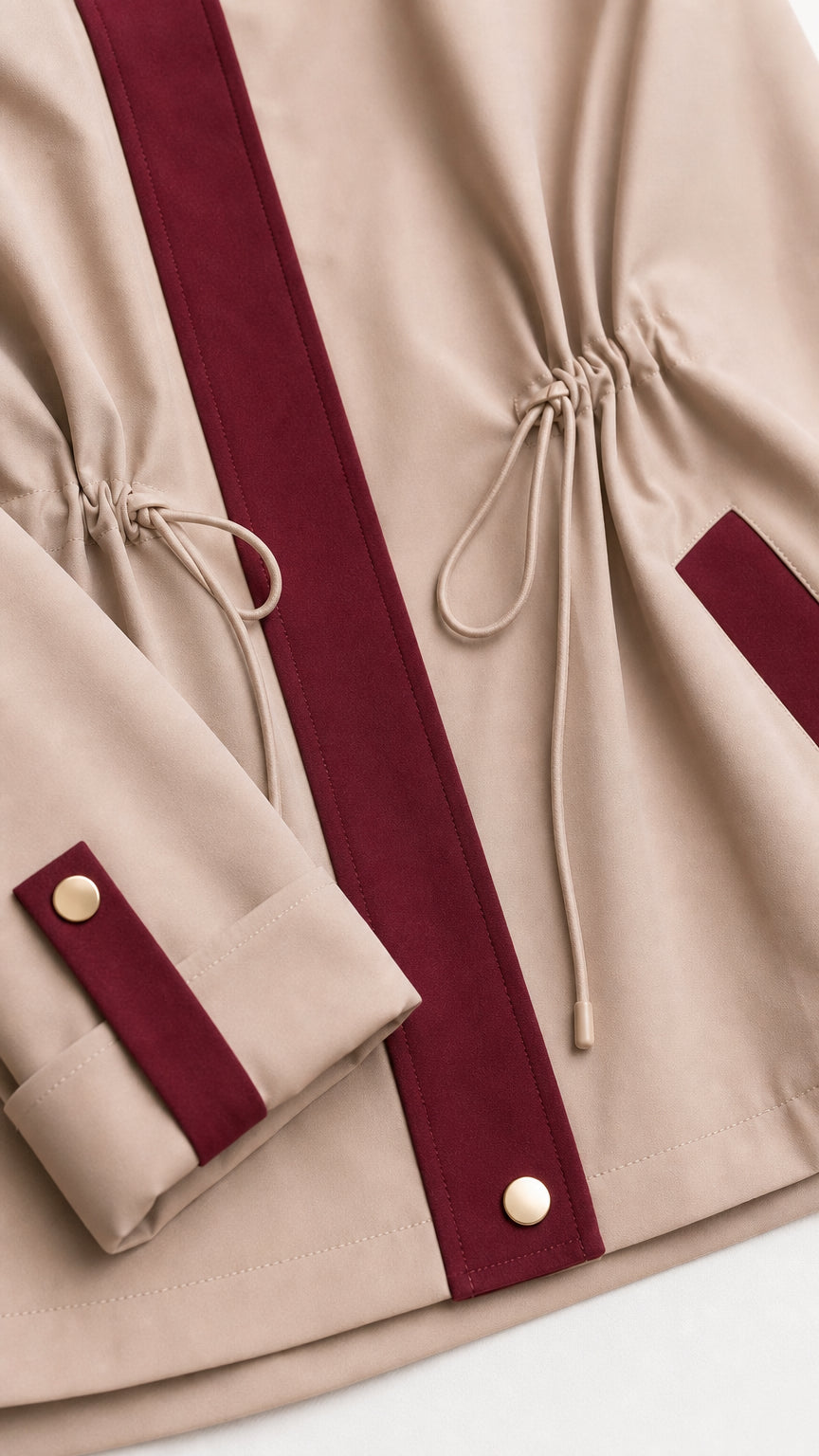 Close-up detail of beige fabric, burgundy contrast placket, drawstring, and button cuff