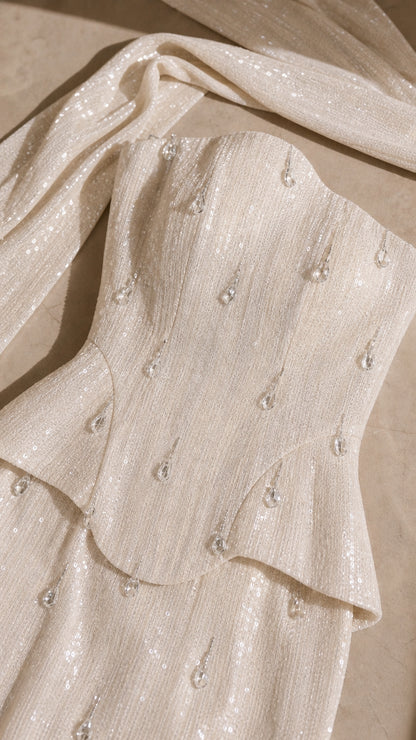 Close-up detail of shimmering sequin fabric, peplum layer, and droplet embellishments
