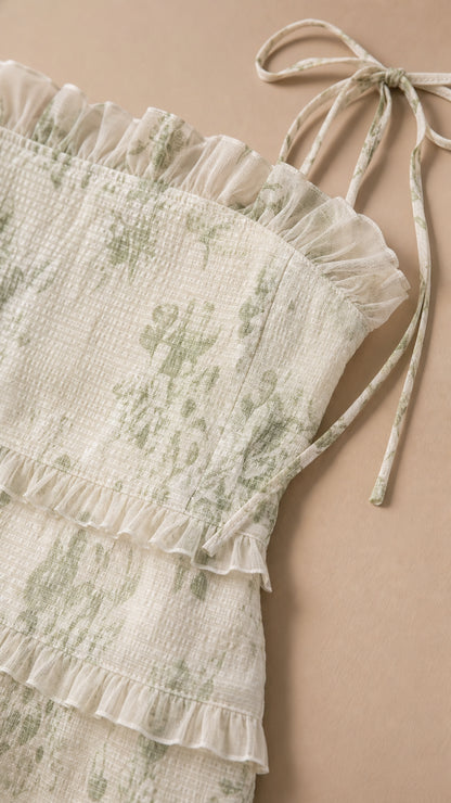 Close-up detail of textured smocking, tiered ruffles, and tie straps in sage green floral