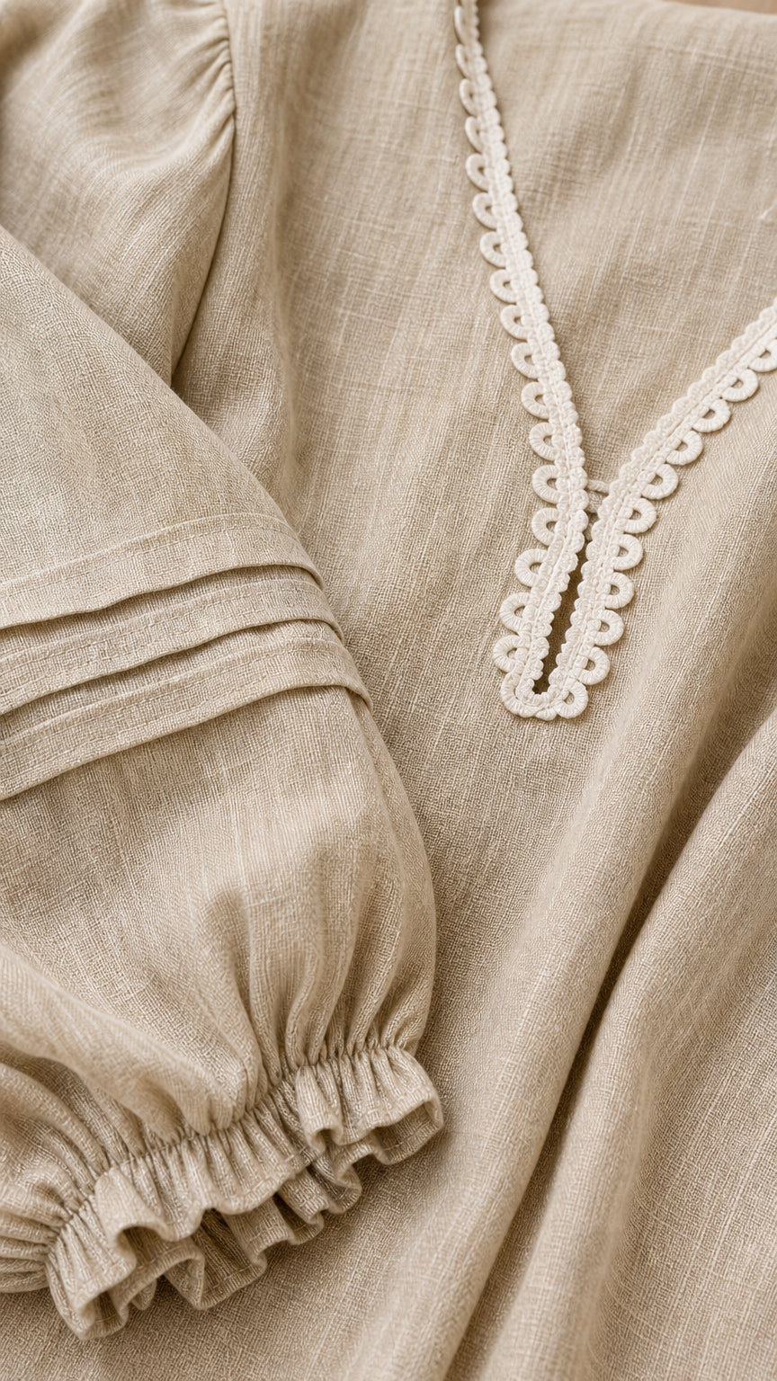 Close-up detail of V-neck lace trim and pleated sleeve on beige dress