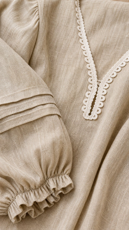Close-up detail of V-neck lace trim and pleated sleeve on beige dress