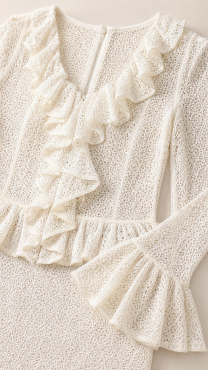 Close-up detail of textured cream lace fabric with ruffle neckline and sleeve cuff