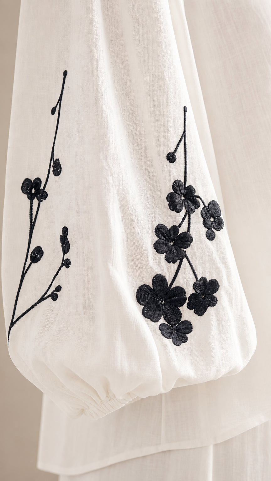 Close-up detail of black floral branch embroidery on white balloon sleeve cuff