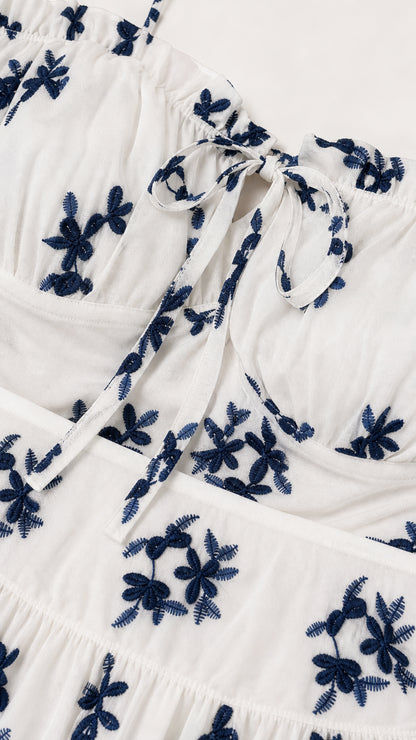 Close-up detail of tie-front neckline and navy floral embroidery on white fabric