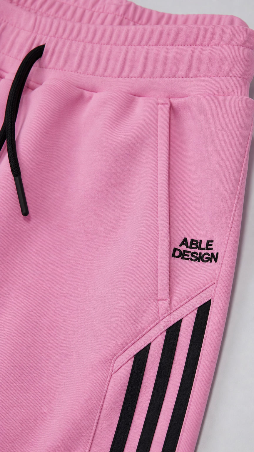 Close up of pink sweatpants waistband, drawstring, pocket, and side stripes