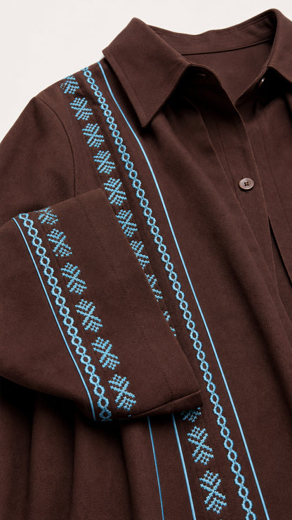 Close-up detail of point collar and cyan geometric embroidery on brown fabric placket and cuff